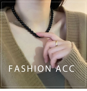 Close-up of black beaded necklace with round lustrous pearls on a brown knit sweater