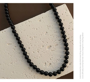 Detailed macro view of elegant black glossy bead necklace on white textured stone background