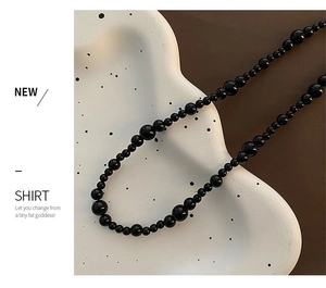 Close-up of black onyx beaded necklace with gradient sizing on a white ceramic stand