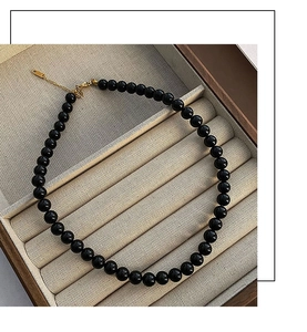 Detailed macro view of black agate beaded necklace with gold clasp in a wooden jewelry box