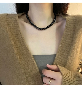 Close-up of minimalist black beaded necklace on model with warm autumn styling