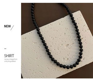 Detail showing polished black bead necklace on textured stone base for an elegant contrast