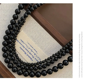 Three layers of polished black bead necklaces with glossy finish on a wooden tray