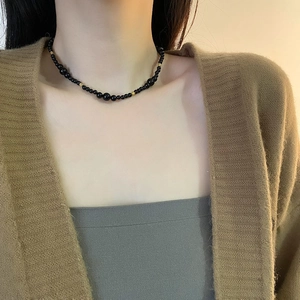 Elegant black onyx beaded necklace with gold accents worn by model on brown knitwear