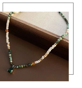 Detail of beaded necklace with green gemstone drop pendant on dark wooden tray