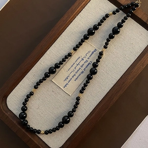 Elegant black onyx beaded necklace with gold hollow spacers on a classic wooden tray