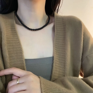 Elegant black beaded necklace with a minimalist gold ring worn on a stylish female model