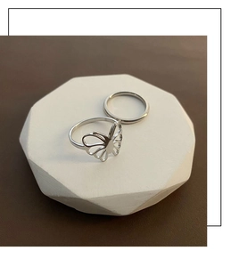 Close-up of polished silver butterfly hollow ring and minimalist band on stone stand