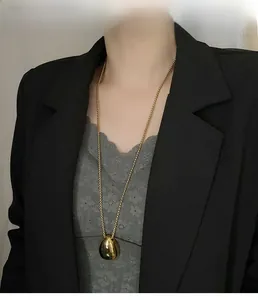 Polished gold teardrop pendant necklace worn over elegant business attire