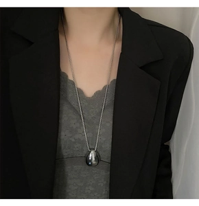 Close-up of a silver polished teardrop pendant necklace on a model with a beaded chain