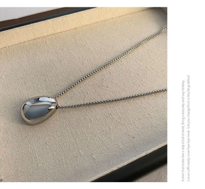 Macro detail of silver teardrop pendant necklace with polished mirror finish on linen