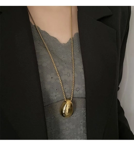 Close-up of polished gold teardrop pendant necklace worn over a black blazer