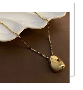 Macro detail of glossy golden teardrop pendant necklace on white ceramic tray