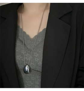 Close-up of a silver teardrop pendant necklace worn with a black blazer for a chic style