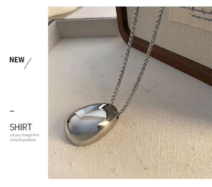 Macro detail of polished teardrop pendant on a beige linen surface with box chain