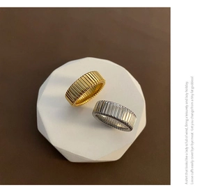 Close-up of gold and silver textured wide band rings on a white stone pedestal