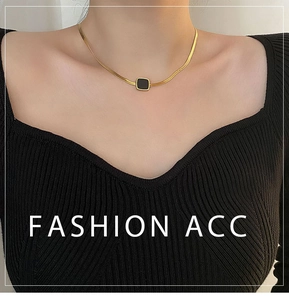 Détail d'un collier chaîne serpent dorée avec pendentif carré noir porté sur un pull noir