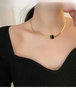 Vue rapprochée du collier chaîne serpent dorée avec pendentif carré noir porté par un modèle
