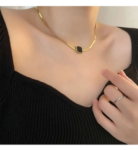 Détail d'un collier chaîne serpent dorée avec pendentif carré noir sur le cou de femme