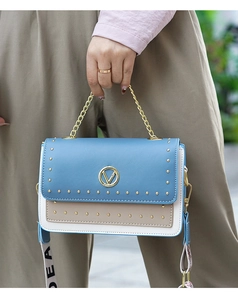 Gros plan d'un sac en cuir patchwork bleu ciel et beige avec rivets dorés et logo V