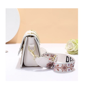 Détail d'un sac bandoulière en cuir blanc avec clous dorés et sangle à motifs chic