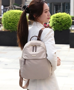 Close-up of beige nylon backpack featuring golden logo plate and brown woven straps