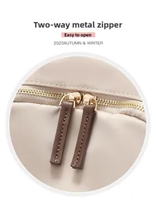 Detail of dual metal zippers on a beige nylon backpack with brown leather pull tabs