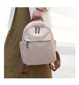 Detail of a beige nylon backpack with brown handles and gold zippers in a street setting