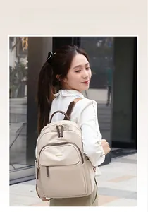 Détail du sac à dos en nylon beige avec finitions en cuir brun et plaque dorée