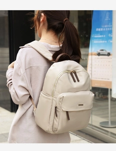 Outdoor street view of a beige nylon backpack with brown leather handle and metal logo