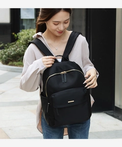 Close-up of black nylon backpack with gold zippers and metal logo in an outdoor street setting