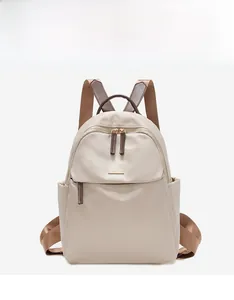 Detail view of smooth beige Oxford fabric backpack with gold metal logo and brown straps