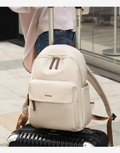 Beige nylon travel backpack resting on a black suitcase handle for travel commuting