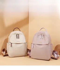 Detail showing beige and lilac oxford fabric backpacks with leather handles and metal logo