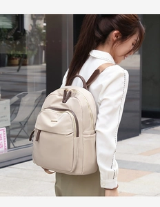Détail du sac à dos en nylon beige avec garniture en cuir marron et plaque de logo dorée
