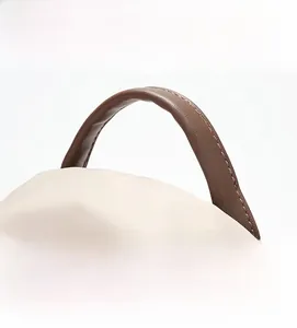 Detail view of the brown leather top handle on a beige nylon travel backpack for women