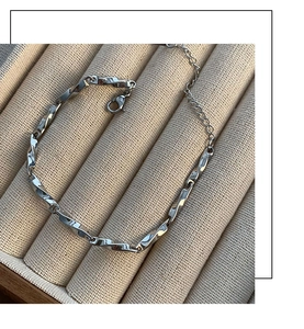 Detail of silver Mobius titanium steel chain bracelet with lobster clasp on beige tray