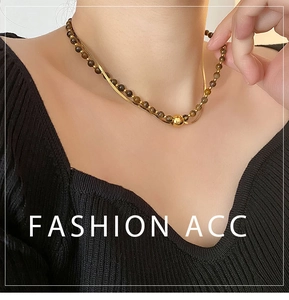 Double-layered gold snake chain and brown tiger eye bead necklace on black sweater