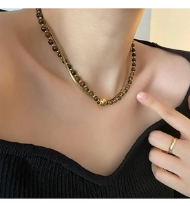 Detail of layered gold snake chain and brown tiger eye bead necklace on a model