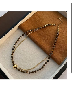 Close-up of double-layer necklace with brown tiger eye beads and gold sphere pendant