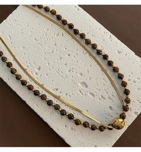 Detail of double-layer necklace with golden snake chain and tiger eye beads on stone