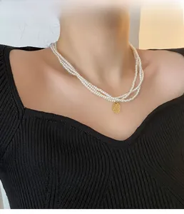 Dettaglio della collana di perle a tre strati con un ciondolo tondo in oro martellato