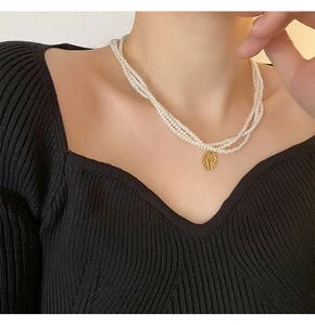 Dettaglio della collana di perle a tre strati con ciondolo a moneta d'oro martellata su modella