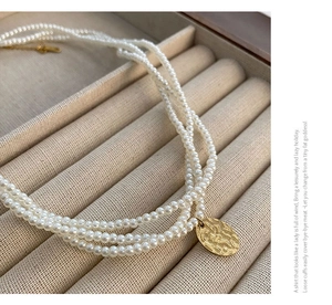 Dettaglio collana di perle a tre strati con pendente martellato dorato su velluto