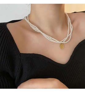Dettaglio della collana di perle a tre strati con un ciondolo rotondo in oro martellato