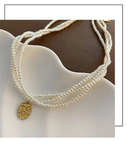 Dettaglio macro di una collana di perle di vetro a tre strati con pendente ovale in oro martellato
