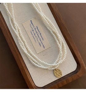 Dettaglio di collana di perle a tre strati con ciondolo in oro martellato in scatola