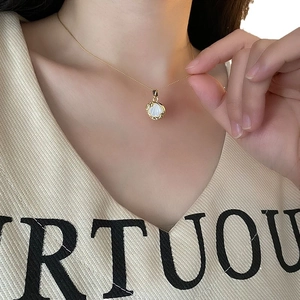 Collier élégant en or avec pendentif rond en nacre blanche porté par le mannequin