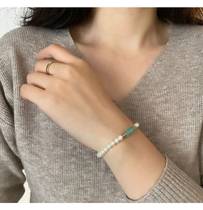 Detail of freshwater pearl bracelet with green beads and gold ring on a model's wrist