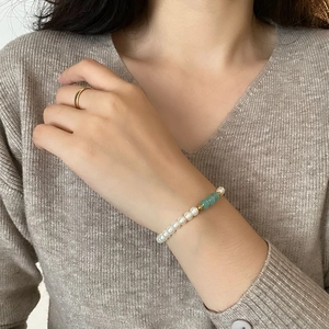 Minimalist titanium steel bracelet with white pearls and green beads on a model's wrist